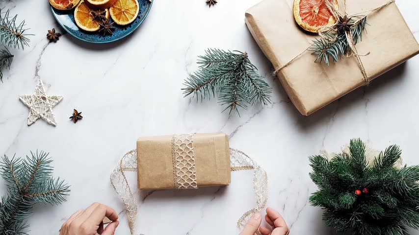 Top view of hands wrapping a gift with lace on a white marble surface.