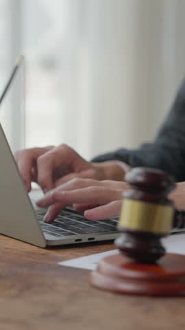Lawyer typing on laptop keyboard at wooden desk with judge gavel in foreground