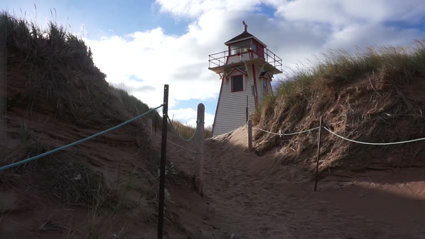 Trucking shot of a lighthouse nestled in the dunes. Morning sun coming over dune grass.