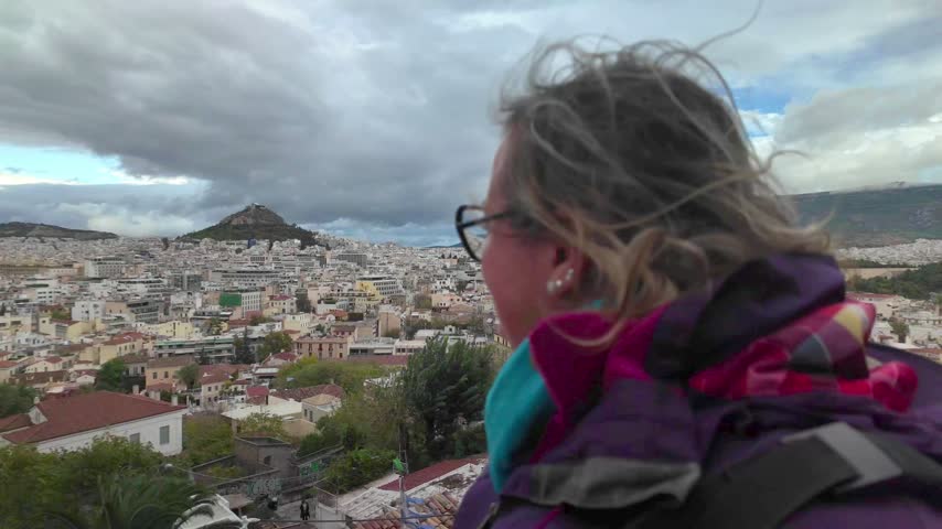 Athens panorama reveals Lycabettus Hill. Panning shot over the city from Anafiotika under dramatic cloudy skies.