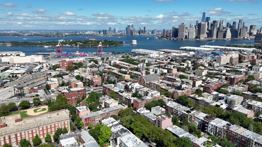 Aerial pan over Red Hook toward Governors Island, the Statue of Liberty and the Lower Manhattan skyline across New York Harbor, Brooklyn, New York City, USA.