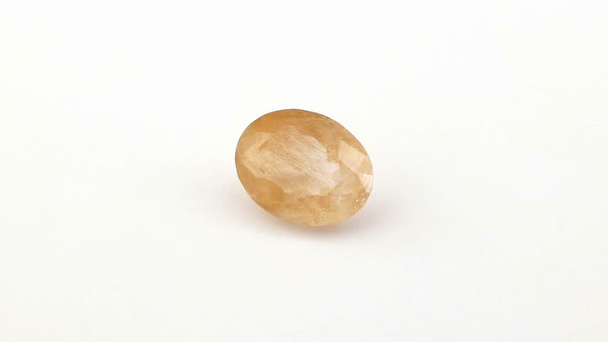 Transparent oval quartz gemstone displaying brilliant golden needle inclusions rotating slowly on a clean white display surface while reflecting light across multiple polished surfaces
