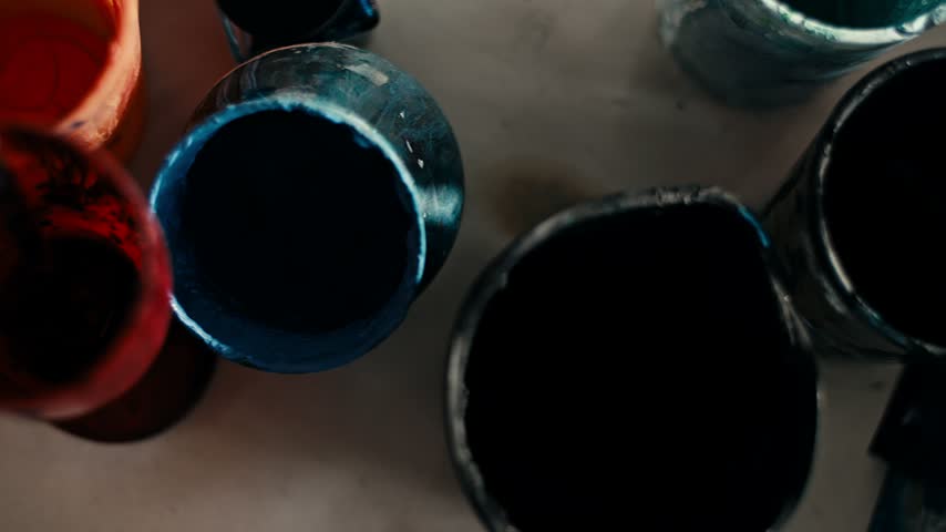 Overhead camera move across cups of orange and dark blue paint with brushes