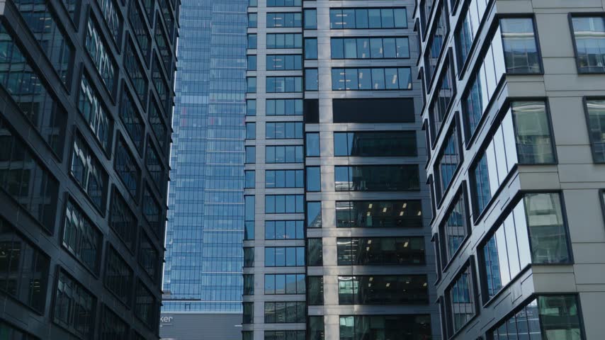 Sunlit modern office building with a glass facade, showing a moving elevator inside. Contemporary architecture in a bustling financial district