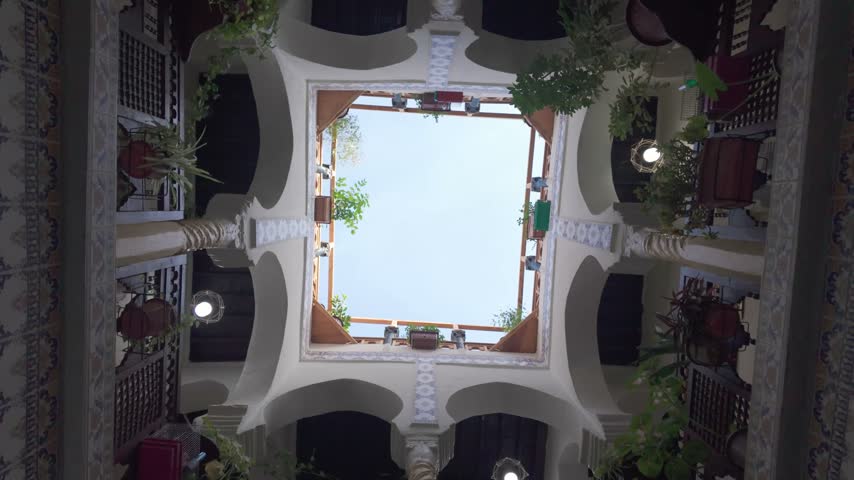 Low angle view moving through a beautiful traditional algerian riad courtyard, revealing ornate architectural details, intricate tilework, arches, and central opening to the sky in casbah of algiers