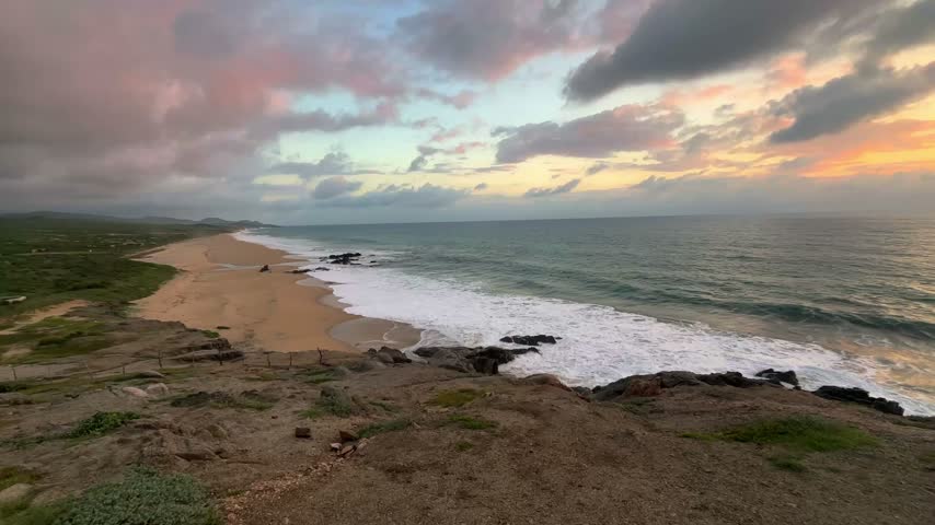 Wide angle view of a pristine sandy beach with crashing ocean waves and colorful sunset clouds in the sky in Baja California Sur, Mexico.