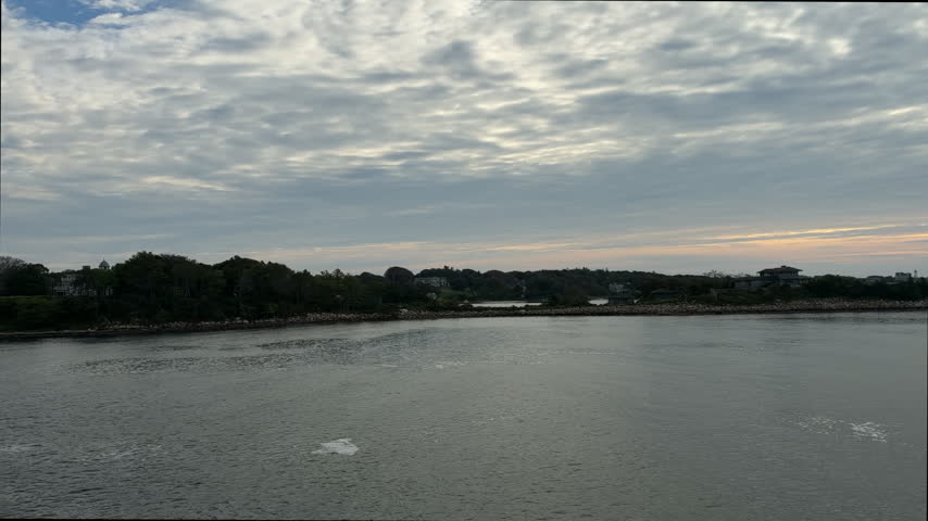 Scenic view of rocky coastline, stone breakwaters, and coastal homes seen from a moving passenger ferry in Cape Cod, Massachusetts