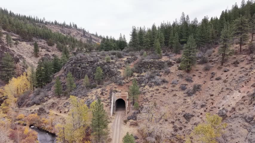 Aerial semi-orbit around a historic railroad tunnel on the Bizz Johnson Trail above the Susan River in Lassen County, California, on an overcast autumn day.