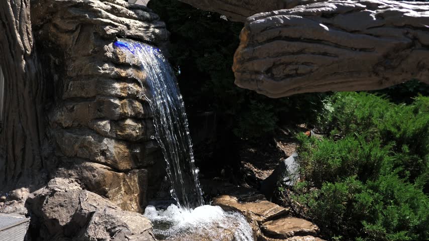 A man-made waterfall in a sun-drenched rock garden, bathed in bright sunlight.