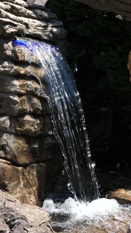 A man-made waterfall in a sun-drenched rock garden, bathed in bright sunlight.