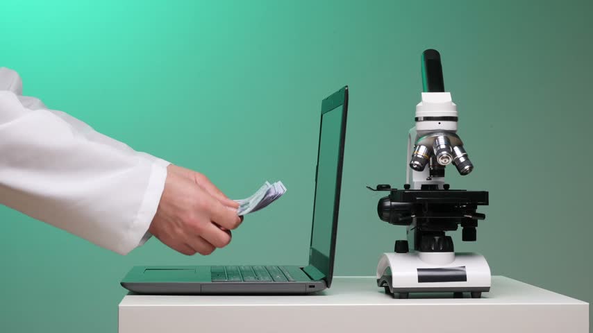 Scientist in lab coat handling cash next to a laptop and a microscope, symbolizing the high costs and necessary funding for scientific advancement and medical research