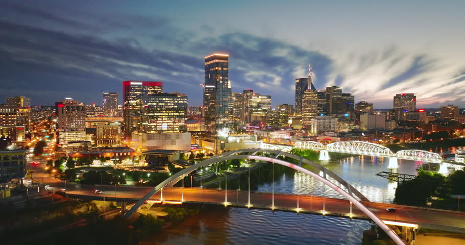 Driving cars on bridge highway near high-rise buildings in downtown district of Nashville, Tennessee, USA. American city with business financial district at night.