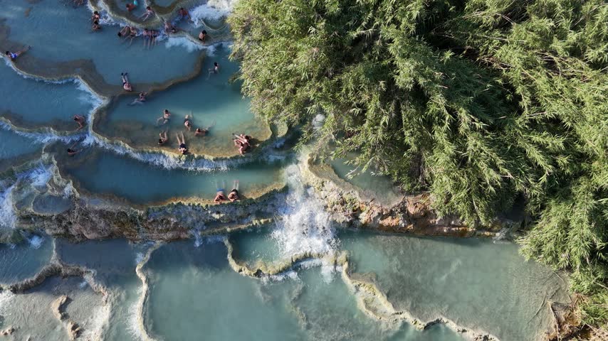 Vertical top-down aerial view capturing the pattern and motion of foaming thermal water flowing through Saturnia