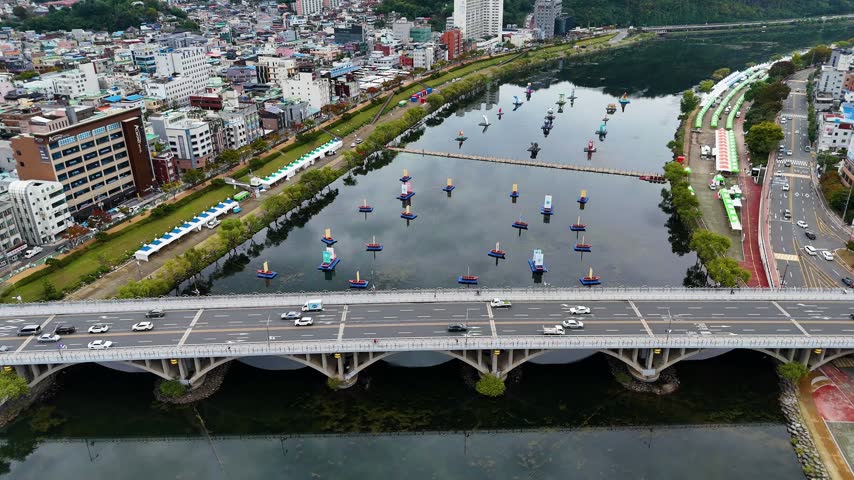 Nam river carrying floating lanterns for the jinju festival while cars drive across the bridge in daytime aerial shot
