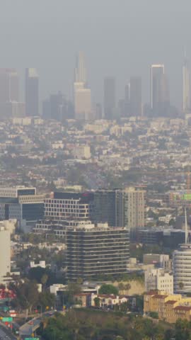 Vertical view of a hazy Hollywood and Los Angeles skyline with a busy freeway, palm trees and Capitol Records tower in warm light, slow camera tilt, Hollywood, Los Angeles, California, USA