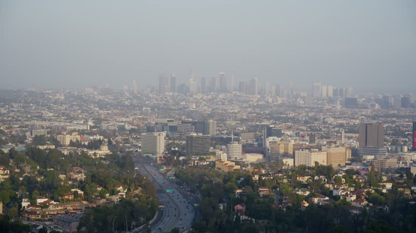 Static view over Hollywood and the downtown Los Angeles skyline in warm haze with a freeway curving through green residential hills, Hollywood, Los Angeles, California, USA