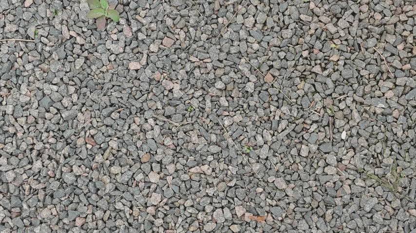 Textured surface of crushed grey stones and pebbles lying on the ground, creating a rough natural pattern outdoors