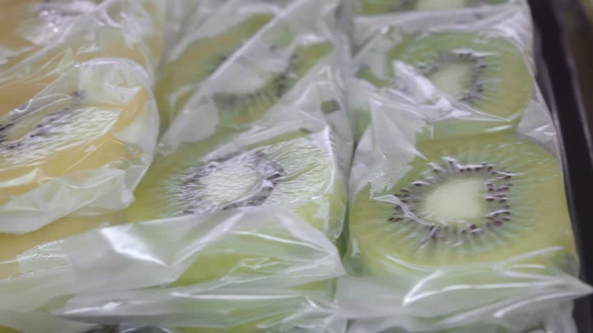 Close up view of prepacked kiwi fruit slices arranged in rows on display shelf in supermarket. Fresh organic produce wrapped in plastic bags ready for sale at grocery store.