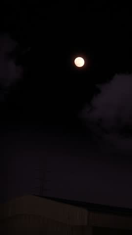 Timelapse of the moon rising with houseware in the foreground and purple sky moving clouds in the background.