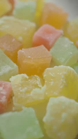 Macro close up footage of translucent multi colored gummy fruit candies scattered on plain white surface. Sweet jelly sugar coated cubes with vibrant soft textures viewed from above.