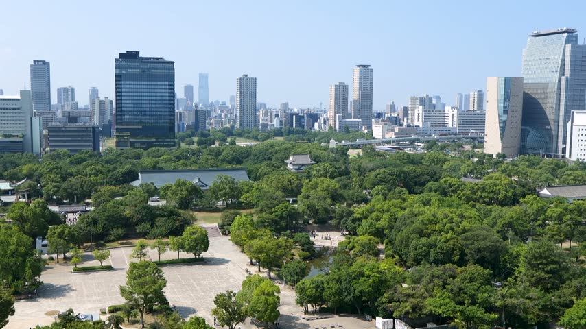 View from Osaka Castle over green park trees and the city skyline on a clear day in Japan