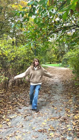Teenage girl standing near trees in autumn park among colorful fall foliage, cozy lifestyle.