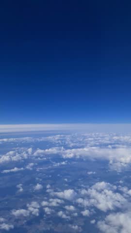 Passenger airplane flying high above fluffy white clouds and green landscape on clear sunny day