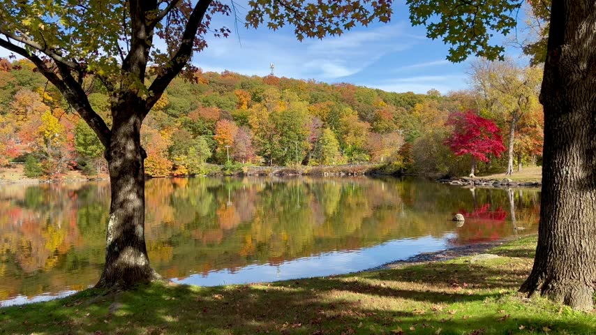 Fall foliage reflects on the calm water of a scenic lake in New England.