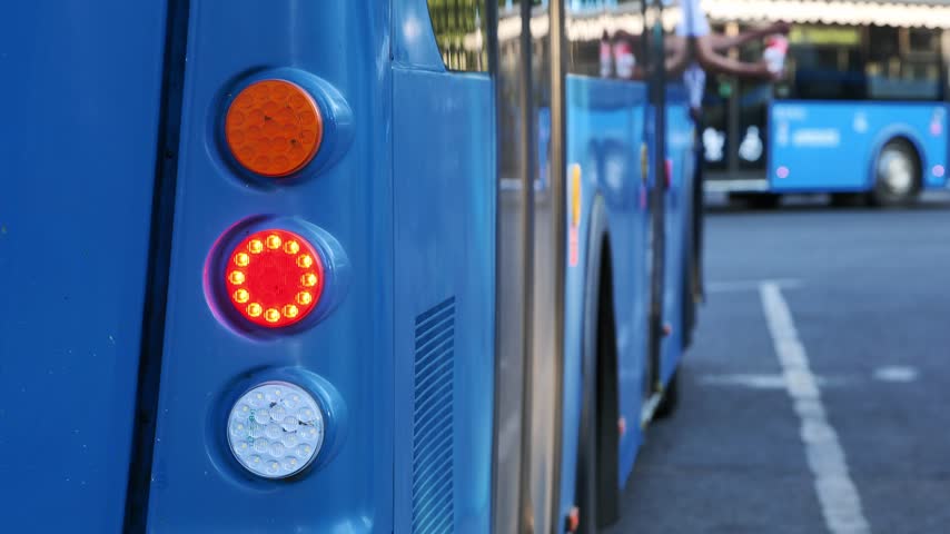 Blue buses lining a city street, with rear lights glowing in urban public transit traffic