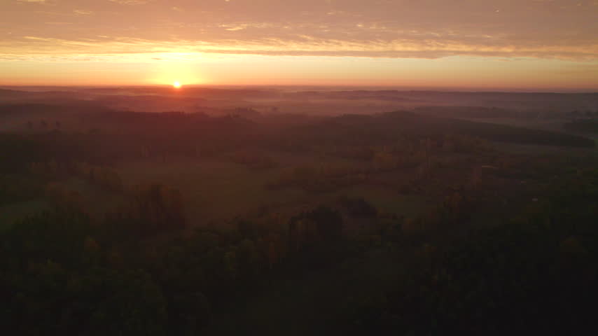 A serene aerial view of a rural landscape during sunrise, capturing the soft glow of the sun over fields and trees