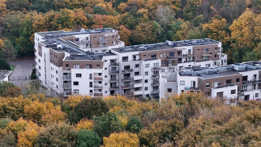 Modern residential apartment building standing surrounded by dense colorful autumn forest