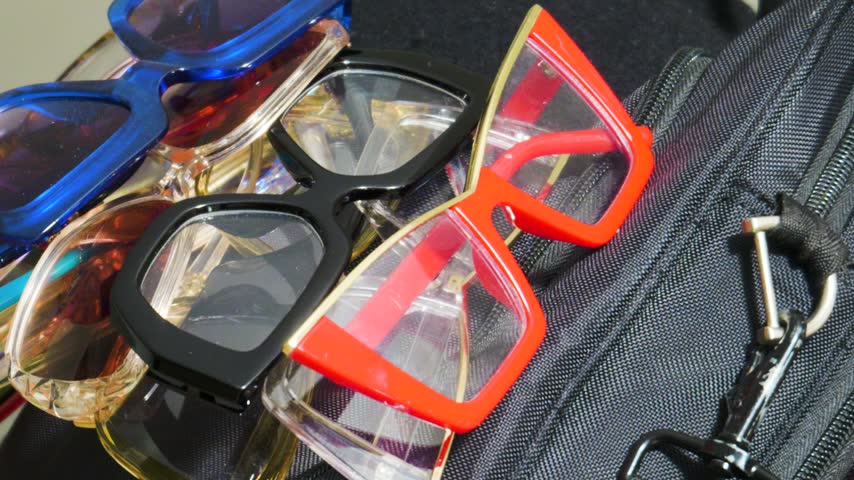 High angle close up view of multiple pairs of vibrant modern sunglasses with plastic frames arranged together on a travel bag.