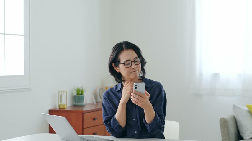 A middle-aged woman thinking while looking at her smartphone.