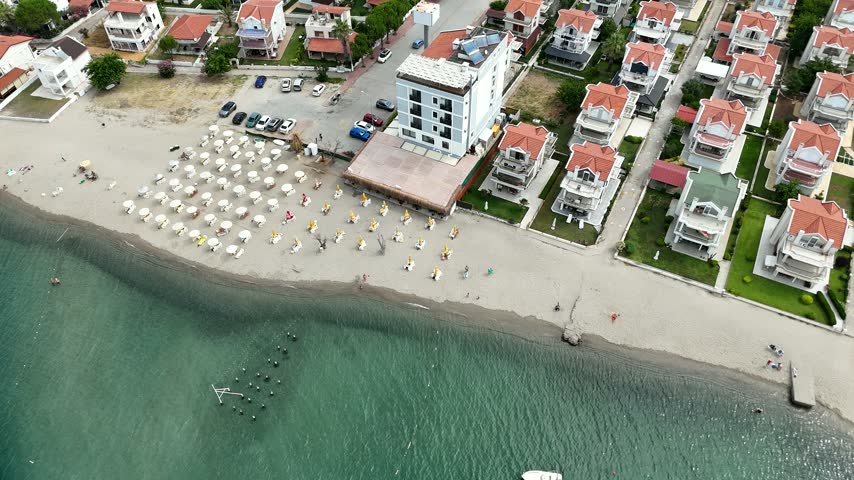 Aerial top view of a sandy beach with sun umbrellas and red roofed summer houses along the Aegean coast in Ayvalik, Turkey