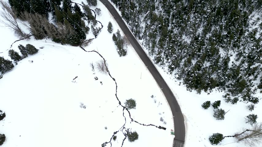 Aerial view of a snowy road winding through a winter forest