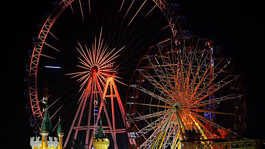 A video of a nighttime scene at an amusement park, featuring two massive, grand-scale Ferris wheels.