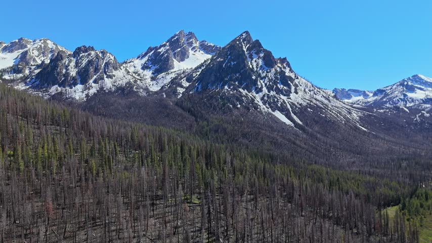 High aerial orbit shot of McGowan Peak at Stanley Lake in Sawtooth National Recreation Area on a sunny day in spring.