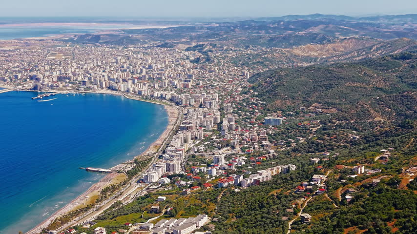 Drone footage of Vlora city, Albania, buildings and streets beside the bay with green hills and deep blue sea in the background