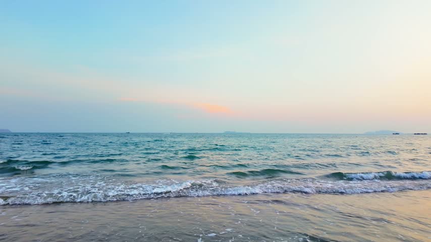 Gentle waves rolling onto a sandy beach at sunset in Sanya