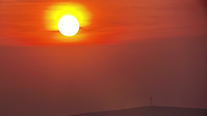 Vibrant sunset with glowing sun over distant hills and warm evening sky