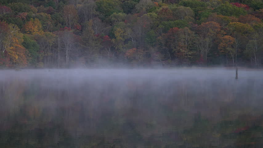 Mystical morning scene of steam fog drifting over Kagami-ike Pond backed by autumn forest