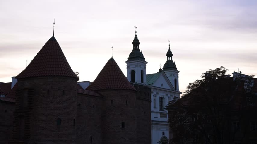 Warsaw Barbican, Historic Semicircular Fortified Outpost With The Church of the Holy Spirit In The Background At Dusk In Warsaw, Poland. Static Shot