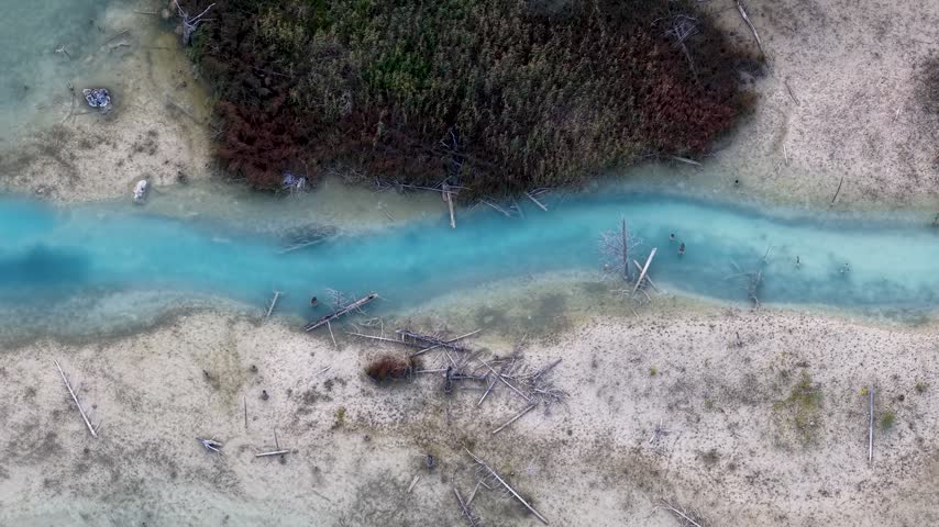 A drone follows a narrow turquoise water channel between pale sandy banks and marsh vegetation near Hessel Michigan