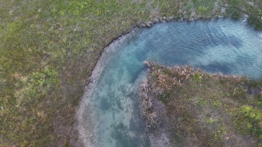 A drone passes above a curved blue water channel surrounded by marsh vegetation near Hessel in Michigans Upper Peninsula