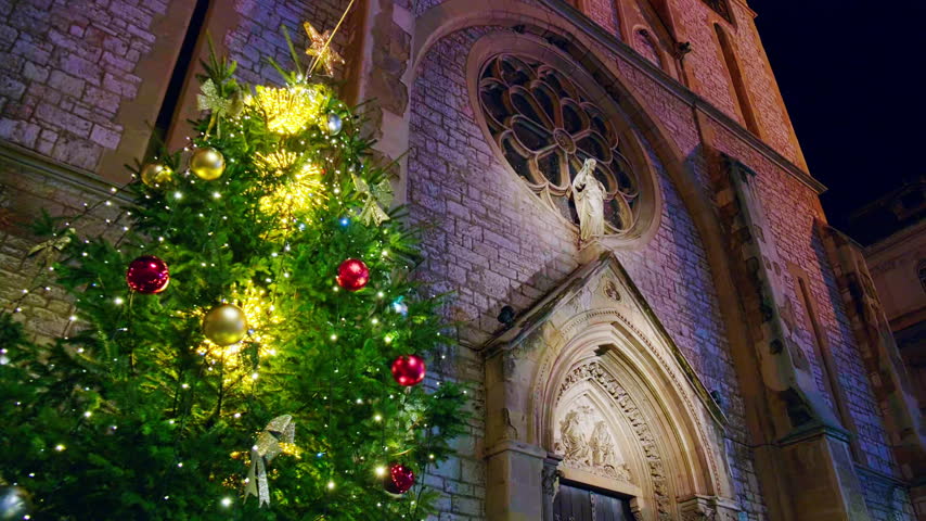 Beautifully decorated Christmas tree illuminated with warm fairy lights and colorful ornaments beside historic Gothic-style church at night. Sacred Heart Cathedral in Sarajevo, Bosnia and Herzegovina