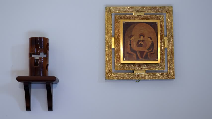 Minimalist chapel interior with a golden framed sacred icon and a small wooden wall shelf on a clean white wall, calm and silent atmosphere
