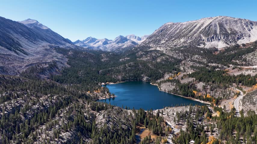 Rock Creek Lake establishing overview of rugged Sierra Nevada peaks, conifer forest and yellow autumn foliage, aerial backdrop, green and grey contrast