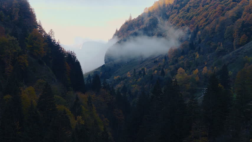 Aerial shot of a rugged alpine mountain massif emerging through thick drifting clouds and mist in Austria, creating a dramatic and atmospheric high mountain landscape.