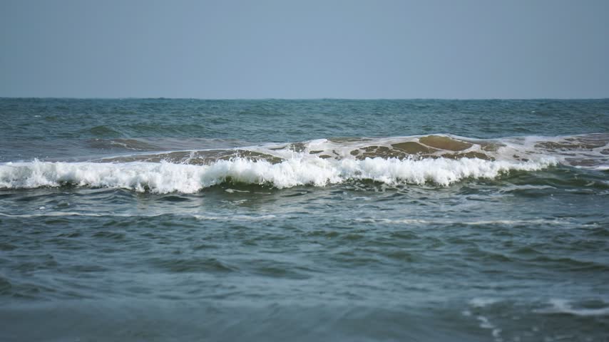 White Foamy Sea Waves Cresting Across Deep Blue Ocean Water Horizontal View. Cresting Sea Waves Line with White Water Foam in Deep Coastal Ocean.