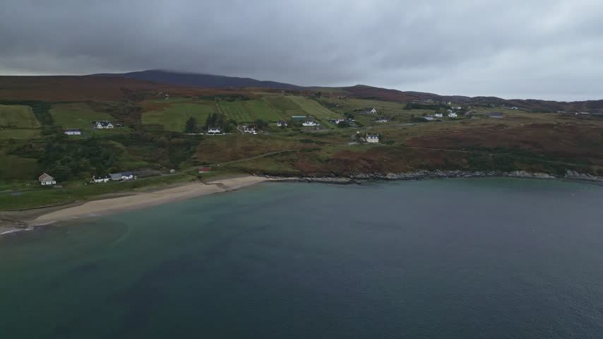 Aerial view of coastal village houses and beach under cloudy skies in rural Scotland
